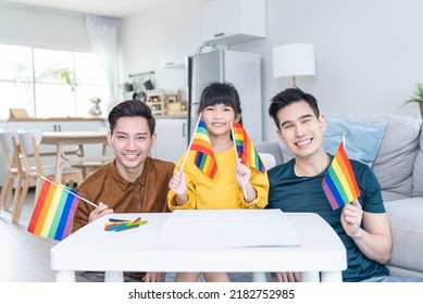 Portrait of Asian LGBTQ men gay family with daughter in living room. Attractive handsome male couple take care and spend time with little cute child holding LGBTQ rainbow flag and looking at camera. - Powered by Shutterstock