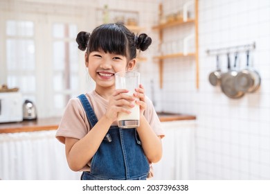 Portrait of Asian little cute kid holding a cup of milk in kitchen in house. Young preschool child girl or daughter stay home with smiling face, feel happy enjoy drinking milk and then look at camera. - Powered by Shutterstock