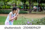 Portrait of asian little girl exploring the nature with magnifying glass outdoors, Child woman playing in the park with magnifying glass. Curious kid exploring nature by magnifier