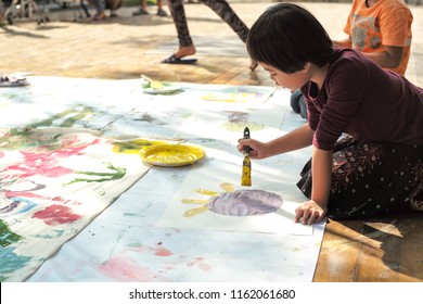 Portrait Asian Little Girl Painting And Drawing On The Paper At Outdoor Art Event For Kids.