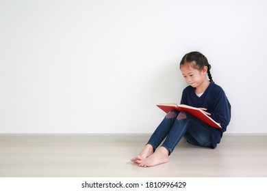 Portrait asian little kid girl in school uniform reading a book and sitting against white wall in the room with copy space. - Shutterstock ID 1810996429
