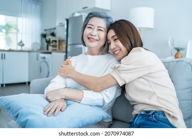 Portrait of Asian lovely family, young daughter hugging older mother. Attractive woman and senior elder mature mom sit on sofa, enjoy activity at home together in living room and smile, look at camera