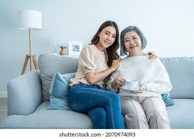 Portrait Of Asian Lovely Family, Young Daughter Hugging Older Mother. Attractive Woman And Senior Elder Mature Mom Sit On Sofa, Enjoy Activity At Home Together In Living Room And Smile, Look At Camera