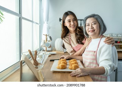 Portrait Of Asian Lovely Family, Young Daughter Stand With Old Mother. Attractive Female And Senior Elderly Mom Wear Apron Enjoy Activity At Home To Bake Croissant In Kitchen And Smile, Look At Camera