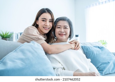 Portrait Of Asian Lovely Family, Young Daughter Hugging Older Mother. Attractive Woman And Senior Elder Mature Mom Sit On Sofa, Enjoy Activity At Home Together In Living Room And Smile, Look At Camera