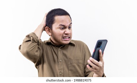 A portrait of an Asian Malay man getting mad and annoying while holding a smartphone on isolated white background. Received bad, failed, unlucky and problem news. Man stressed out over the phone.