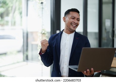 Portrait Of An Asian Male Business Owner Standing With A Computer Showing Happiness After A Successful Investment.