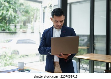 Portrait Of An Asian Male Business Owner Standing Using A Computer To Analyze Work.