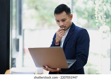 Portrait Of An Asian Male Business Owner Standing Using A Computer To Analyze Work.