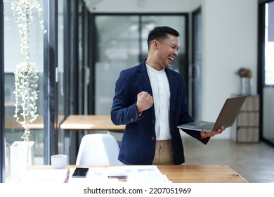 Portrait Of An Asian Male Business Owner Standing With A Computer Showing Happiness After A Successful Investment.