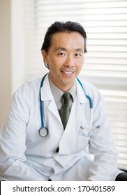 Portrait Of Asian Male Cancer Specialist With Stethoscope Around Neck Sitting In Hospital