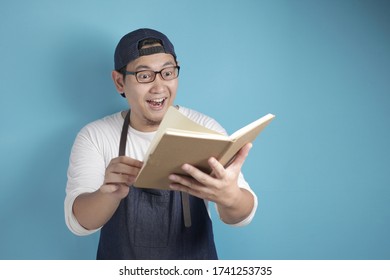 Portrait Of Asian Male Chef Reading Book Of Recipes, Finding Secret Recipe, Against Blue Background