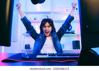 Portrait of Asian male gamer celebrating victory in front of the gaming table. Gamer winning an esports game with victory emotion. The player rejoices in victory in the competition.