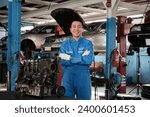 Portrait of Asian male mechanic supervisor in uniform, arms crossed and looking at camera near car engine at service garage, happy maintenance work, check and repair occupation in automotive industry.