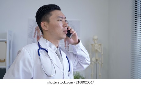 Portrait Asian Male Physician Is Receiving A Phone Call And Talking With A Serious Look By The Window In His Office.