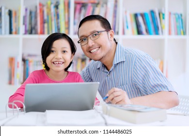 Portrait Of Asian Male Teacher Smiling At The Camera While Using A Laptop With His Student In The Library