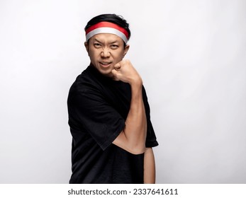 A portrait of an Asian man celebrating Independence Day, wearing a black shirt and a red and white headband, showing a strong gesture by lifting his arms and flexing his muscles. Isolated with a white