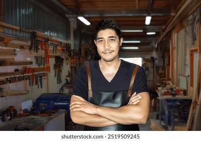 Portrait asian man crossed arm wearing apron on carpenter garage background in wood furniture creator concept