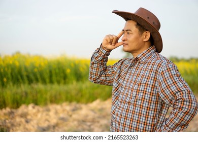 Portrait Of Asian Man Farmer Is At Garden, Wears Hat And Plaid Shirt, Thinking Something At Garden, Feels Serious. Concept : Farmer Think And Plan About Agriculture. Agricultural Occupation.          