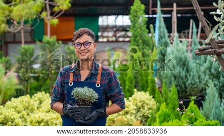 Portrait of Asian man gardener caring potted plants and flowers in greenhouse garden. Male plant shop owner working with houseplants in store. Small business entrepreneur and plant caring concept