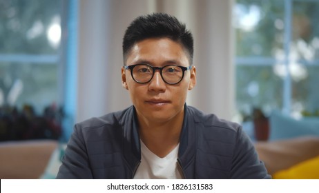 Portrait of asian man in glasses talking online via video call sitting at home. Guy freelancer talking to customer having video conference from home. Korean guy chatting with friends online