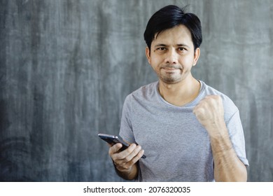 Portrait Asian Man Holding Smartphone And Showing Triumphant Expression