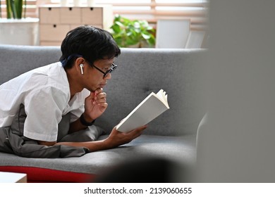 A Portrait Of Asian Man Laying Down On A Couch Reading A Book, For Lifestyle, Education And Home Concept.