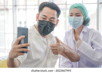 Portrait Of Asian Man Selfie By Phone At While Getting Covid Vaccine In Clinic Or Hospital, With Hand Nurse Injecting Vaccine To Get Immunity For Protect Virus. People Wearing Protective Mask.