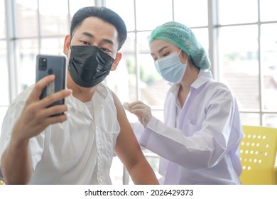 Portrait Of Asian Man Selfie By Phone At While Getting Covid Vaccine In Clinic Or Hospital, With Hand Nurse Injecting Vaccine To Get Immunity For Protect Virus. People Wearing Protective Mask.