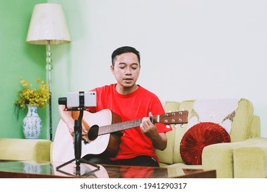 Portrait Of Asian Man Singing And Playing A Guitar While Recording By Smart Phone At Home 