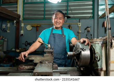 Portrait of an Asian man smiling. Senior craftsman who is skilled in craftsmanship, is controlling, skillfully operating a lathe, is in a small factory that is his family business. - Powered by Shutterstock