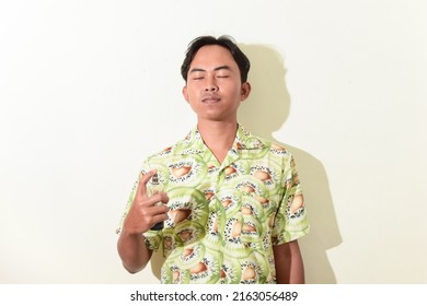 Portrait Of Asian Man Spraying Perfume On His Body. Indonesian Man In Hawaiian Shirt On White Background Isolated. Cool And Handsome Asian Man Portrait