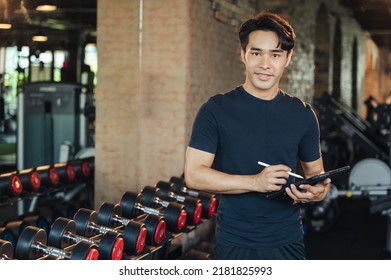 Portrait Asian Man Trainer Using Tablet In Weights Room At Fitness Gym. Workout Training In Fitness Gym.