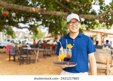 Portrait of Asian man waiter serving food and drink to customer on the table at tropical beach cafe and restaurant on summer holiday vacation. Food and drink business service occupation concept. - Powered by Shutterstock