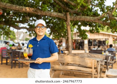 Portrait of Asian man waiter serving food and drink to customer on the table at tropical beach cafe and restaurant on summer holiday vacation. Food and drink business service occupation concept. - Powered by Shutterstock