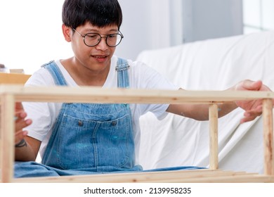 Portrait Of Asian Man Wear White T-shirt With Bear Suit Sitting Assemble Shelves In New Apartment, Renovation Concept 