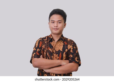 Portrait of Asian man wearing batik shirt keeping arms crossed and smiling at camera. Isolated image on gray background