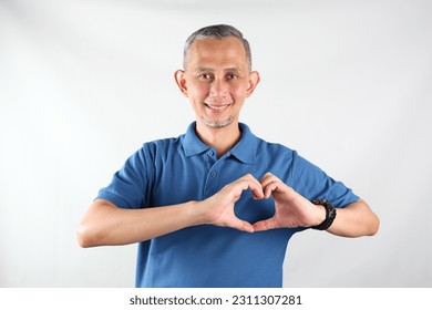 Portrait of Asian man wearing blue tshirt smiling with love sign (heart with fingers) on his chest, health concept.
 - Shutterstock ID 2311307281