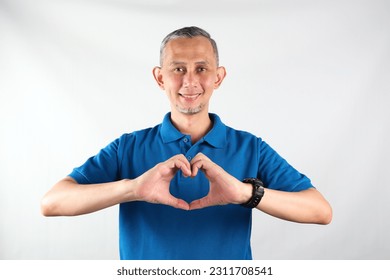 Portrait of Asian man wearing blue tshirt smiling with love sign (heart with fingers) on his chest, health concept.
 - Shutterstock ID 2311708541