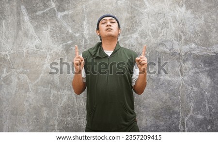 Portrait of asian man wearing green and taqiyah (cap) on cement background show gesture belive in one god . Islamic religious photo concept