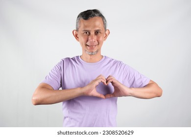 Portrait of Asian Man wearing purple tshirt smiling with love sign (heart with fingers) on his chest, health concept.
 - Shutterstock ID 2308520629