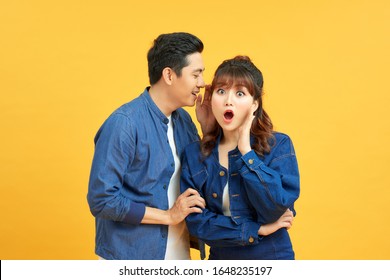 Portrait of asian man whispering secret or interesting gossip to excited woman in her ear isolated over yellow background - Powered by Shutterstock