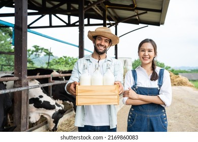 Portrait Of Asian Man And Woman Dairy Farmer Holding Milk In Cowshed. Attractive Agricultural Farmer People Smile And Looking At Camera After Milking The Cow With Happiness At Livestock Farm Industry.