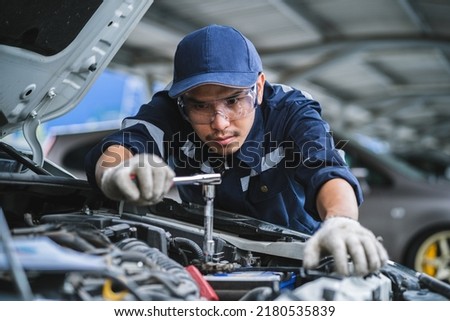 Portrait of an Asian mechanic checking the safety of a car. Maintenance of damaged parts in the garage. Maintenance repairs. Repair service concept.