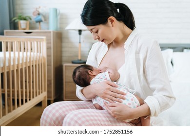 portrait of asian millennial mother breast feeding her baby. taiwanese new mom experiencing pure joy watching her child in arms. breastfeeding promotion concept