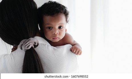 portrait of asian mother and her black mixed race baby girl in white room