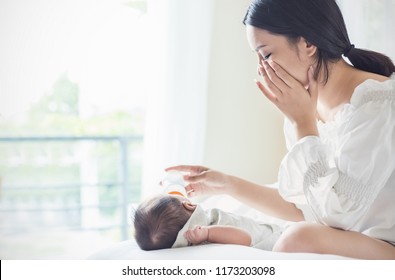 Portrait Of Asian Mother Nursery Feeding Bottle Of Formula Milk To Newborn Baby In Bed Crying Suffering From Post Natal Depression. Health Care Breastfeeding Single Mom Motherhood Stressful Concept.