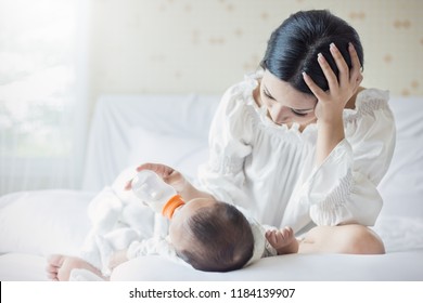 Portrait Of Asian Mother Nursery Feeding Bottle Of Formula Milk To Newborn Baby In Bed Suffering From Post Natal Depression. Health Care Single Mom Motherhood Stressful Concept.