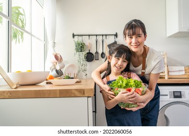 Portrait Of Asian Mother Stand With Daughter And Hold Vegetables Bowl. Happy Family, Attractive Parent Mom And Young Little Girl Child Look At Camera And Smile Enjoy Healthy Foods In Kitchen At Home.