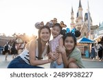 Portrait of Asian mother and two daughter traveling in the theme park. Happy family, attractive woman and children feel happy and relax, spend time for vacation at amusement park and look at camera.